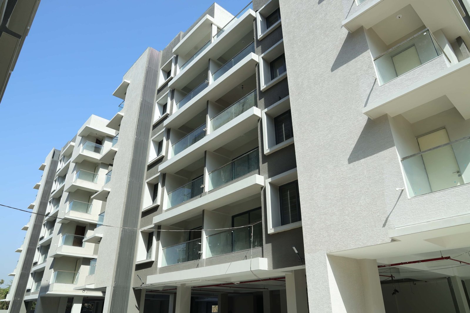 - Front elevation of Arise Ample low-rise luxury apartments on S.G. Highway, Ahmedabad - Solar panels and energy-efficient fixtures integrated on the rooftop of Arise Ample residences - Dramatic fenestration pattern across the monotone façade of Arise Ample apartments - Achromatic color scheme with bold planes and shaded tints on the Arise Ample exterior - Landscaped courtyard promoting healthy living at the environmentally friendly Arise Ample complex
