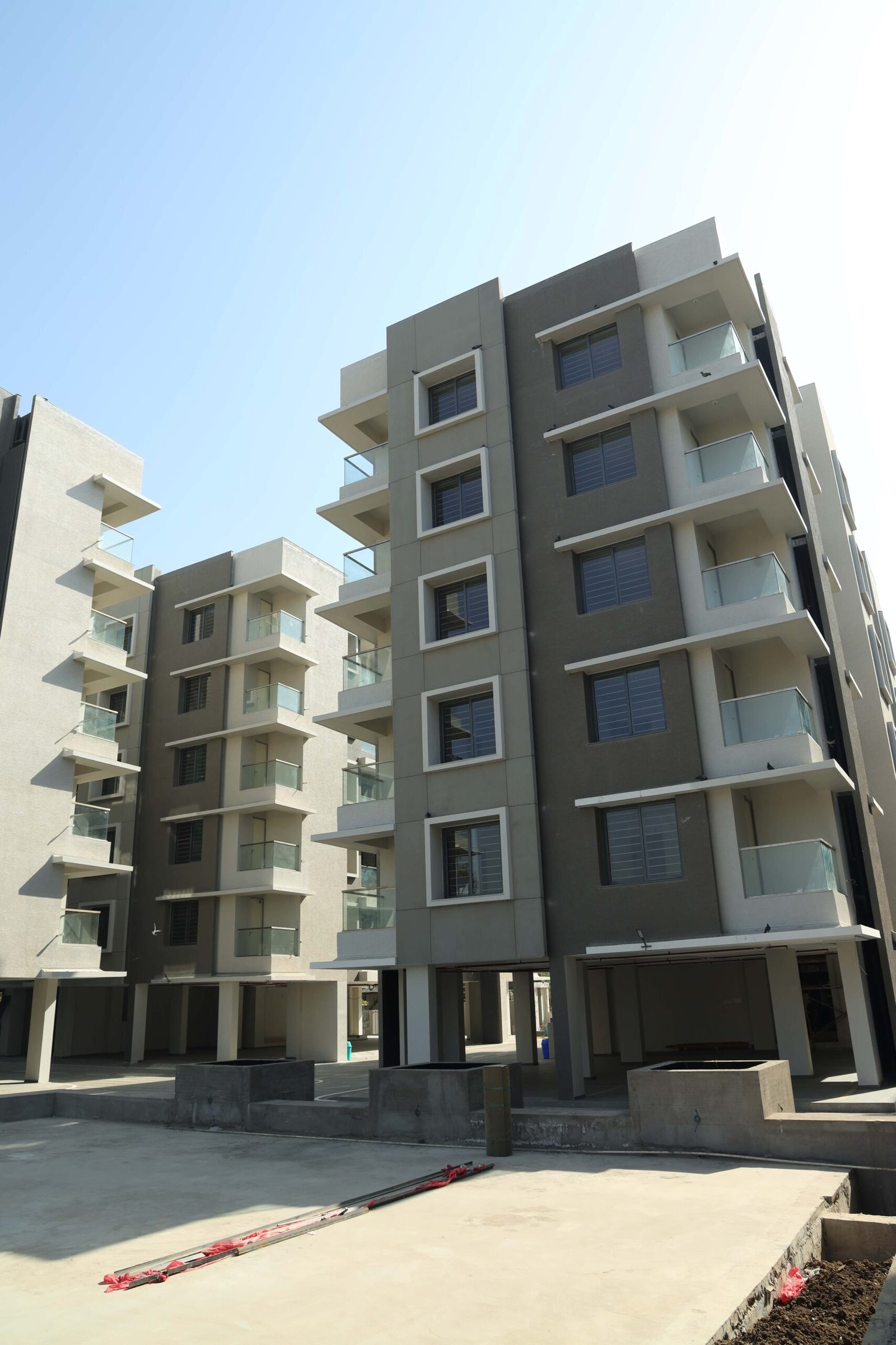 - Front elevation of Arise Ample low-rise luxury apartments on S.G. Highway, Ahmedabad - Solar panels and energy-efficient fixtures integrated on the rooftop of Arise Ample residences - Dramatic fenestration pattern across the monotone façade of Arise Ample apartments - Achromatic color scheme with bold planes and shaded tints on the Arise Ample exterior - Landscaped courtyard promoting healthy living at the environmentally friendly Arise Ample complex