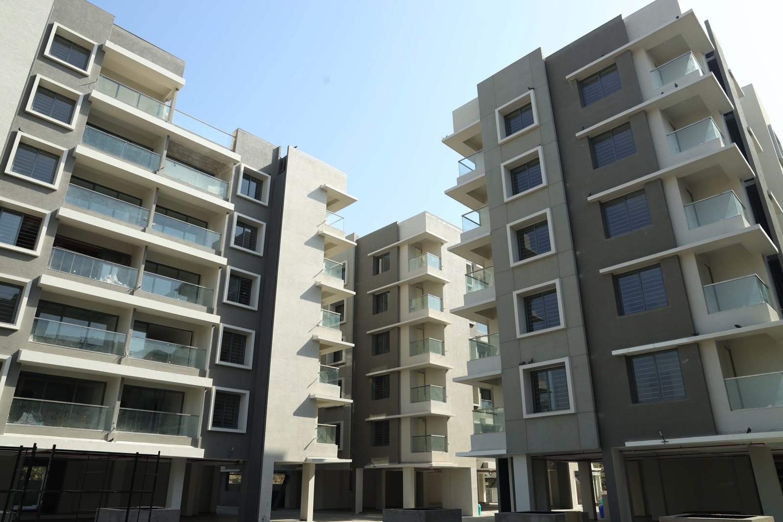 - Front elevation of Arise Ample low-rise luxury apartments on S.G. Highway, Ahmedabad - Solar panels and energy-efficient fixtures integrated on the rooftop of Arise Ample residences - Dramatic fenestration pattern across the monotone façade of Arise Ample apartments - Achromatic color scheme with bold planes and shaded tints on the Arise Ample exterior - Landscaped courtyard promoting healthy living at the environmentally friendly Arise Ample complex