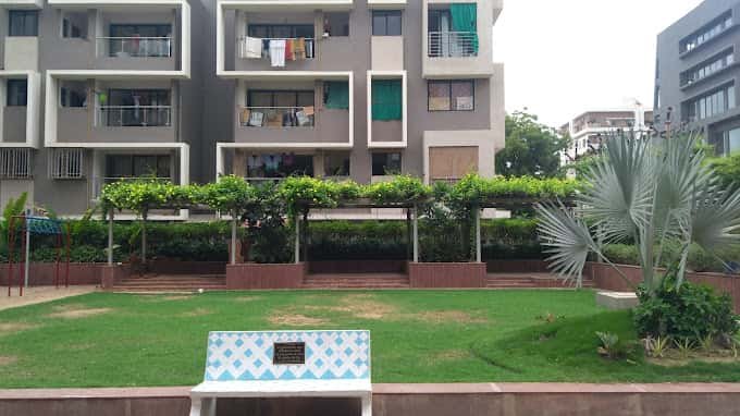 - Front elevation of the 4-storey Arise Icon building with landscaped courtyard and ramp access - Interior of a 2 BHK apartment at Arise Icon highlighting open-plan living and built-in storage - 3 BHK unit at Arise Icon with floor-to-ceiling glazing and seamless flow between rooms - Universal-access pathway and seating nook in Arise Icon’s outdoor garden - Rooftop terrace at Arise Icon featuring greenery, seating pods, and city views - Exterior view of Arise Pride’s minimalist 3 BHK residential tower on S.G. Highway - Open-plan living room in a 3 BHK apartment at Arise Pride with sleek finishes - Corridors and circulation spaces in Arise Pride showcasing efficient layout planning - Child-friendly landscaped play area within Arise Pride’s grounds - Shaded garden path and seating benches for seniors at Arise Pride complex