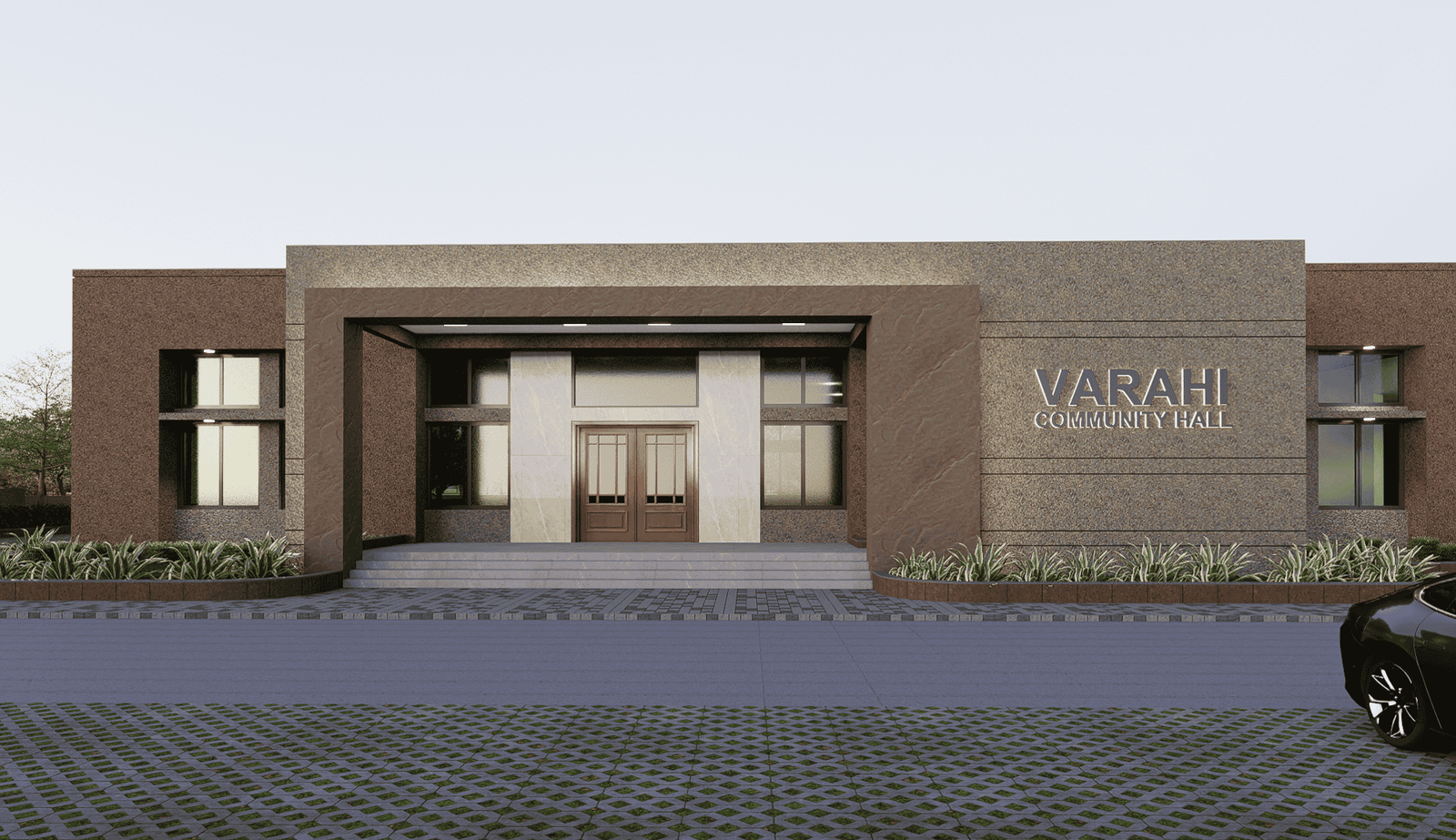 - Exterior view of Varahi Community Hall showcasing a welcoming entrance canopy, local decorative motifs, and landscaped forecourt - Interior shot of the main hall with a flexible open layout, movable seating stacks, and stage area ready for events - Festive gathering inside the hall with residents seated around long tables, colorful decorations, and natural light filtering through clerestory windows - Close-up of ornamental wall patterns and exposed wooden beams that reflect Varahi’s cultural craftsmanship - Night-time façade illuminated by warm uplights, highlighting the building’s form and its integration with surrounding greenery
