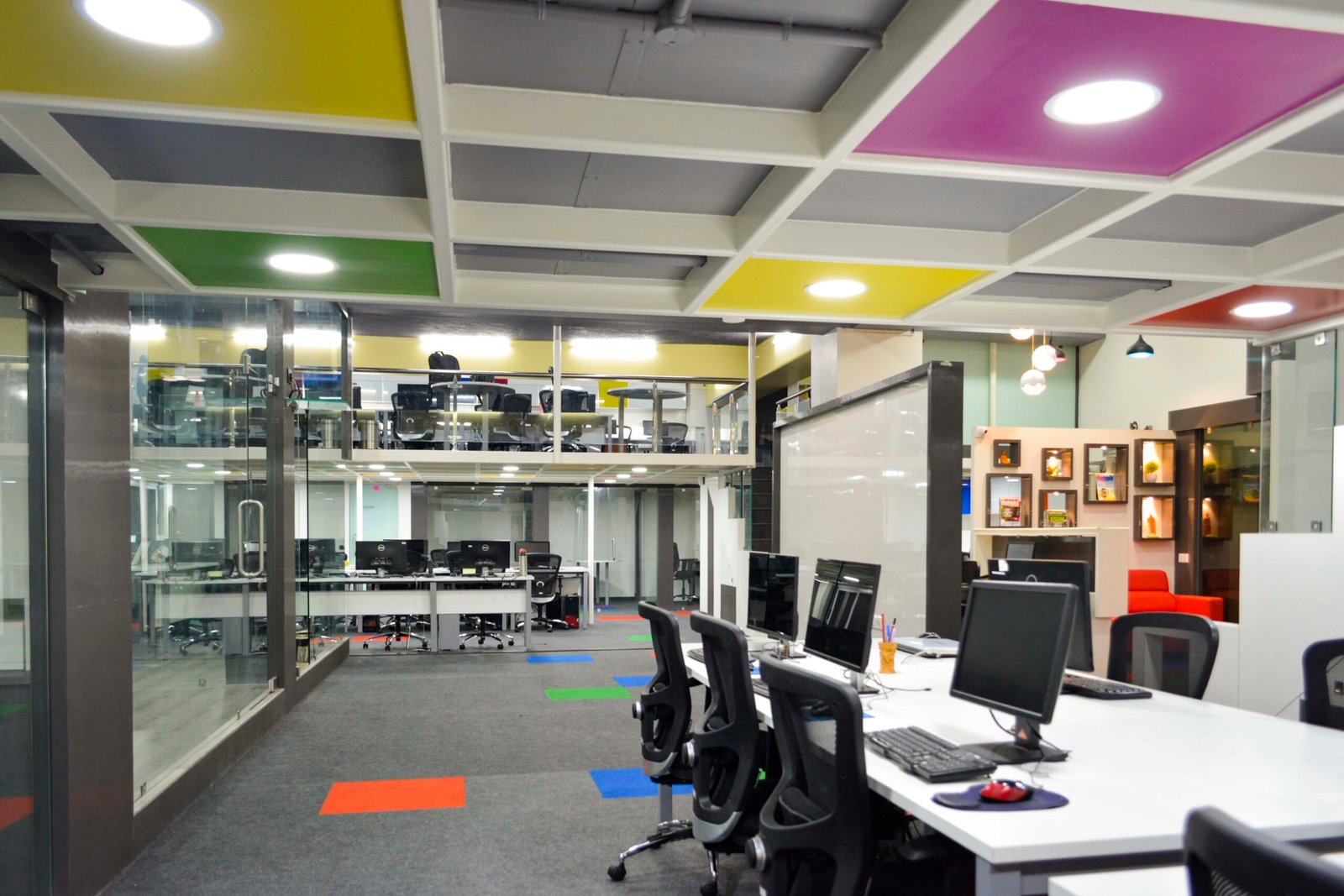 - Entrance view of MultiDots Office showcasing a vibrant reception area with colourful wall graphics - Open-plan workstation with ergonomic desks and bright accent lighting - Collaborative breakout zone featuring informal seating pods and dynamic wall art - Smart conference room equipped with large digital screens and modern furnishings - Relaxation corner with lounge chairs and greenery creating a calm retreat