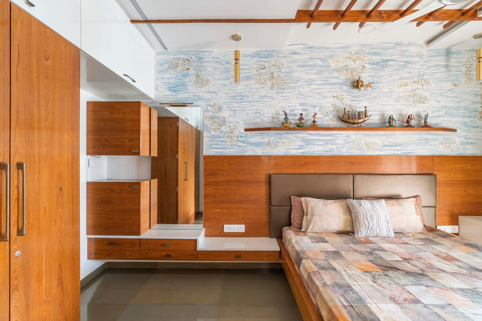 - Modern bungalow facade with exposed concrete, stone cladding, and wooden louvers in Ahmedabad - Sandstone-clad entrance with illuminated staircase and landscaped exterior - Open-plan living and dining area with geometric partition and modern chandelier - Master bedroom with blue textured wallpaper, wooden ceiling grid, and floating bedside units - Guest bedroom with geometric headboard, floating desk, and accent lighting - Polished flooring, natural wood finishes, and integrated lighting in modern residential interior