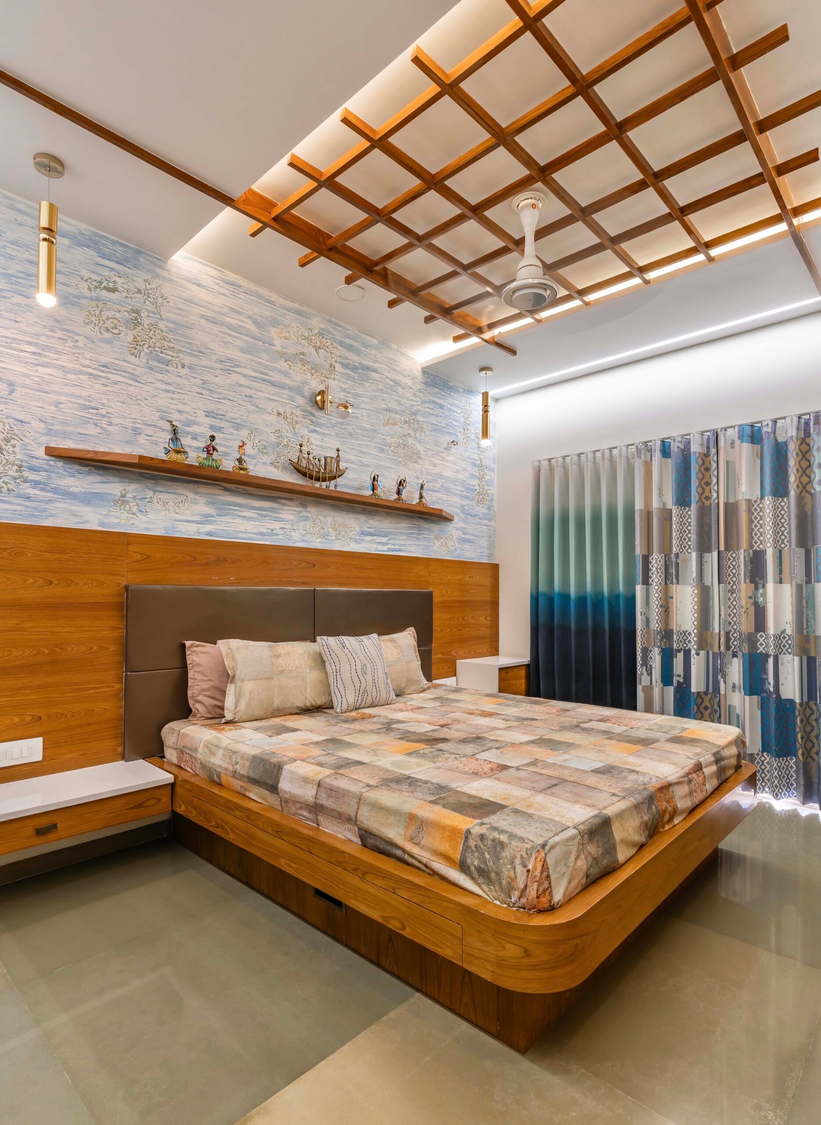 - Modern bungalow facade with exposed concrete, stone cladding, and wooden louvers in Ahmedabad - Sandstone-clad entrance with illuminated staircase and landscaped exterior - Open-plan living and dining area with geometric partition and modern chandelier - Master bedroom with blue textured wallpaper, wooden ceiling grid, and floating bedside units - Guest bedroom with geometric headboard, floating desk, and accent lighting - Polished flooring, natural wood finishes, and integrated lighting in modern residential interior