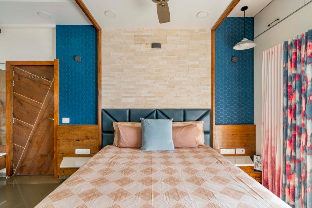 - Modern bungalow facade with exposed concrete, stone cladding, and wooden louvers in Ahmedabad - Sandstone-clad entrance with illuminated staircase and landscaped exterior - Open-plan living and dining area with geometric partition and modern chandelier - Master bedroom with blue textured wallpaper, wooden ceiling grid, and floating bedside units - Guest bedroom with geometric headboard, floating desk, and accent lighting - Polished flooring, natural wood finishes, and integrated lighting in modern residential interior