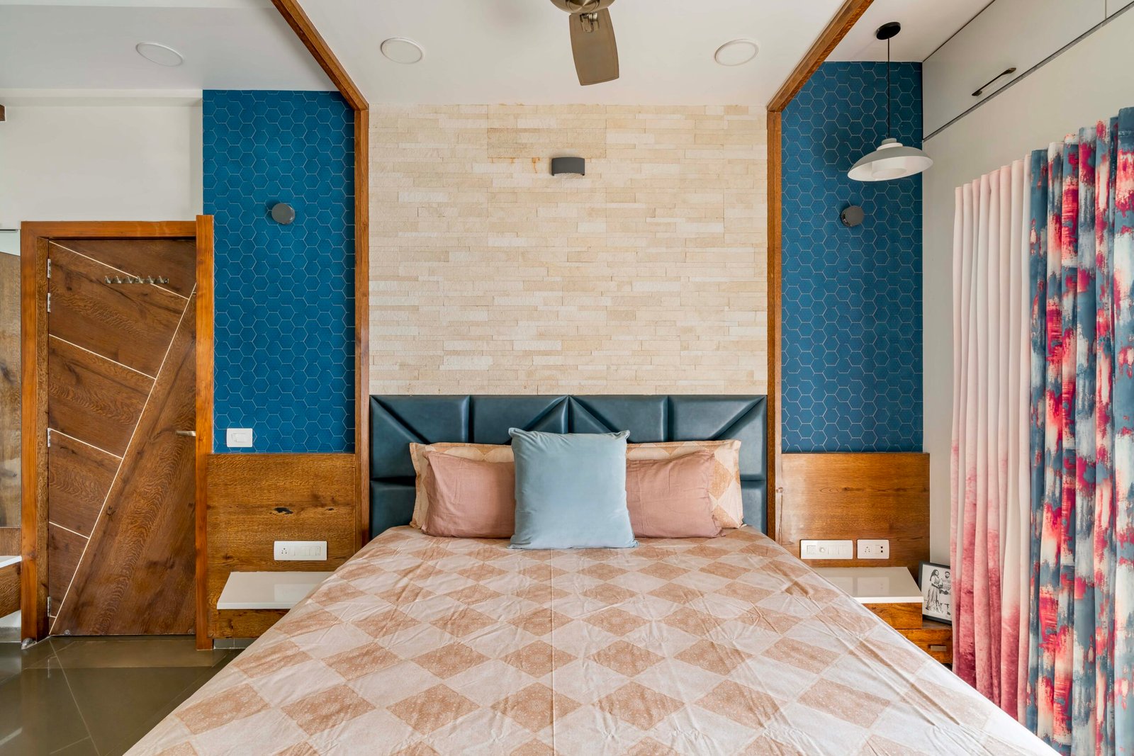 - Modern bungalow facade with exposed concrete, stone cladding, and wooden louvers in Ahmedabad - Sandstone-clad entrance with illuminated staircase and landscaped exterior - Open-plan living and dining area with geometric partition and modern chandelier - Master bedroom with blue textured wallpaper, wooden ceiling grid, and floating bedside units - Guest bedroom with geometric headboard, floating desk, and accent lighting - Polished flooring, natural wood finishes, and integrated lighting in modern residential interior