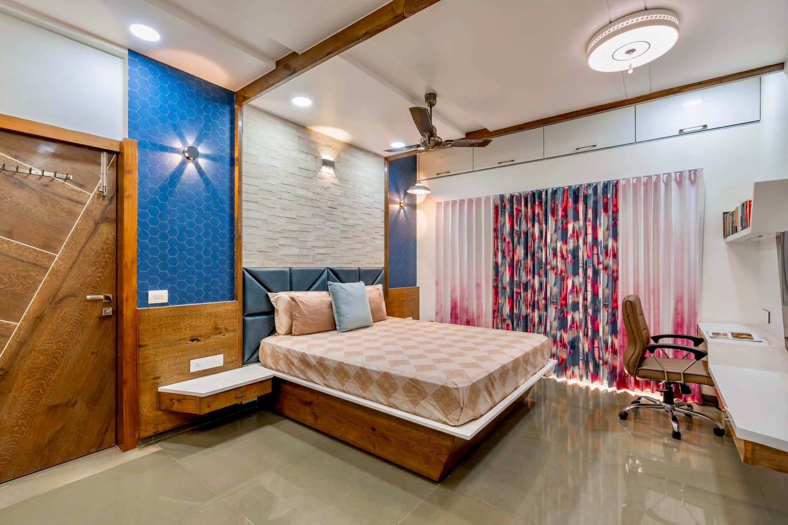 - Modern bungalow facade with exposed concrete, stone cladding, and wooden louvers in Ahmedabad - Sandstone-clad entrance with illuminated staircase and landscaped exterior - Open-plan living and dining area with geometric partition and modern chandelier - Master bedroom with blue textured wallpaper, wooden ceiling grid, and floating bedside units - Guest bedroom with geometric headboard, floating desk, and accent lighting - Polished flooring, natural wood finishes, and integrated lighting in modern residential interior
