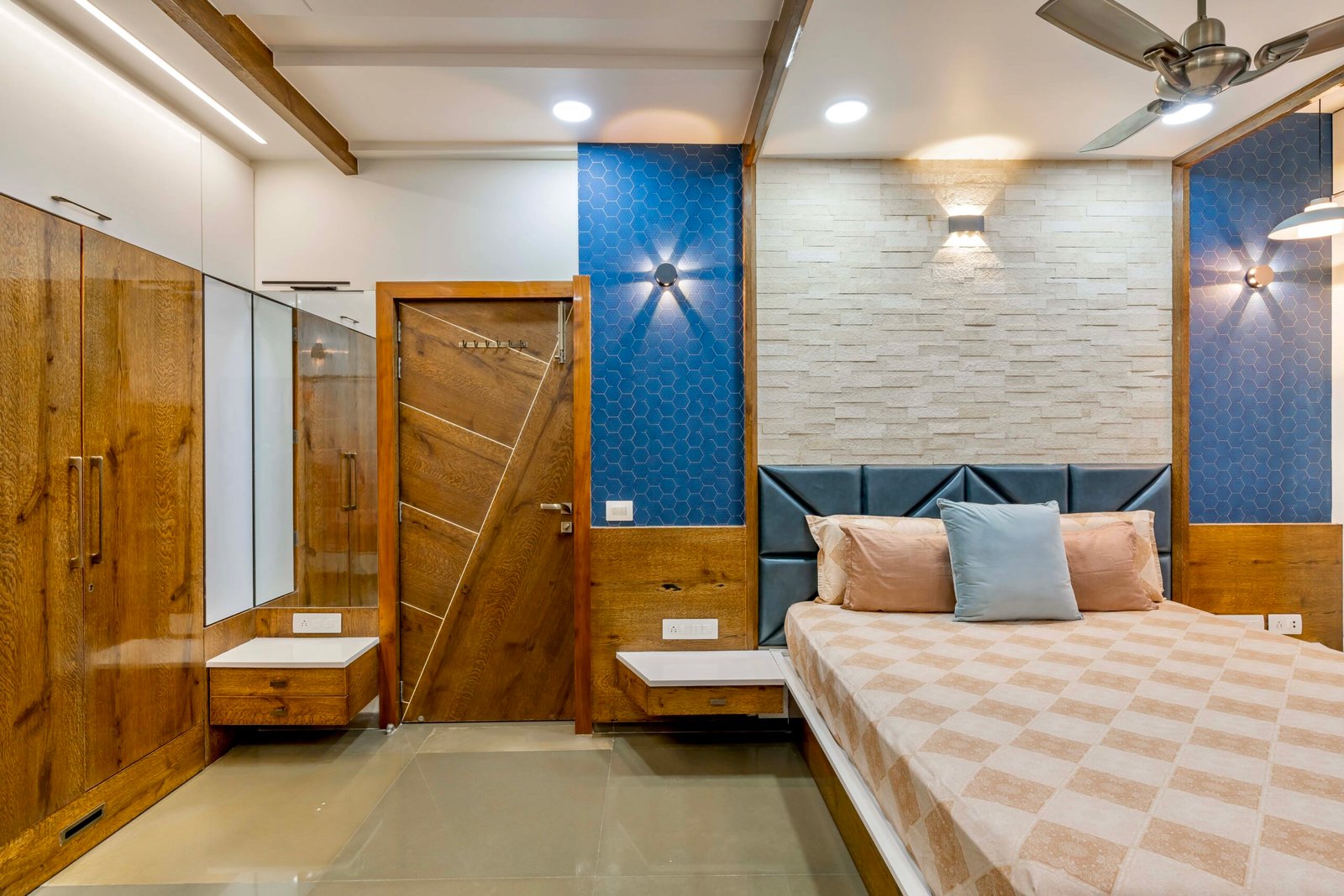 - Modern bungalow facade with exposed concrete, stone cladding, and wooden louvers in Ahmedabad - Sandstone-clad entrance with illuminated staircase and landscaped exterior - Open-plan living and dining area with geometric partition and modern chandelier - Master bedroom with blue textured wallpaper, wooden ceiling grid, and floating bedside units - Guest bedroom with geometric headboard, floating desk, and accent lighting - Polished flooring, natural wood finishes, and integrated lighting in modern residential interior