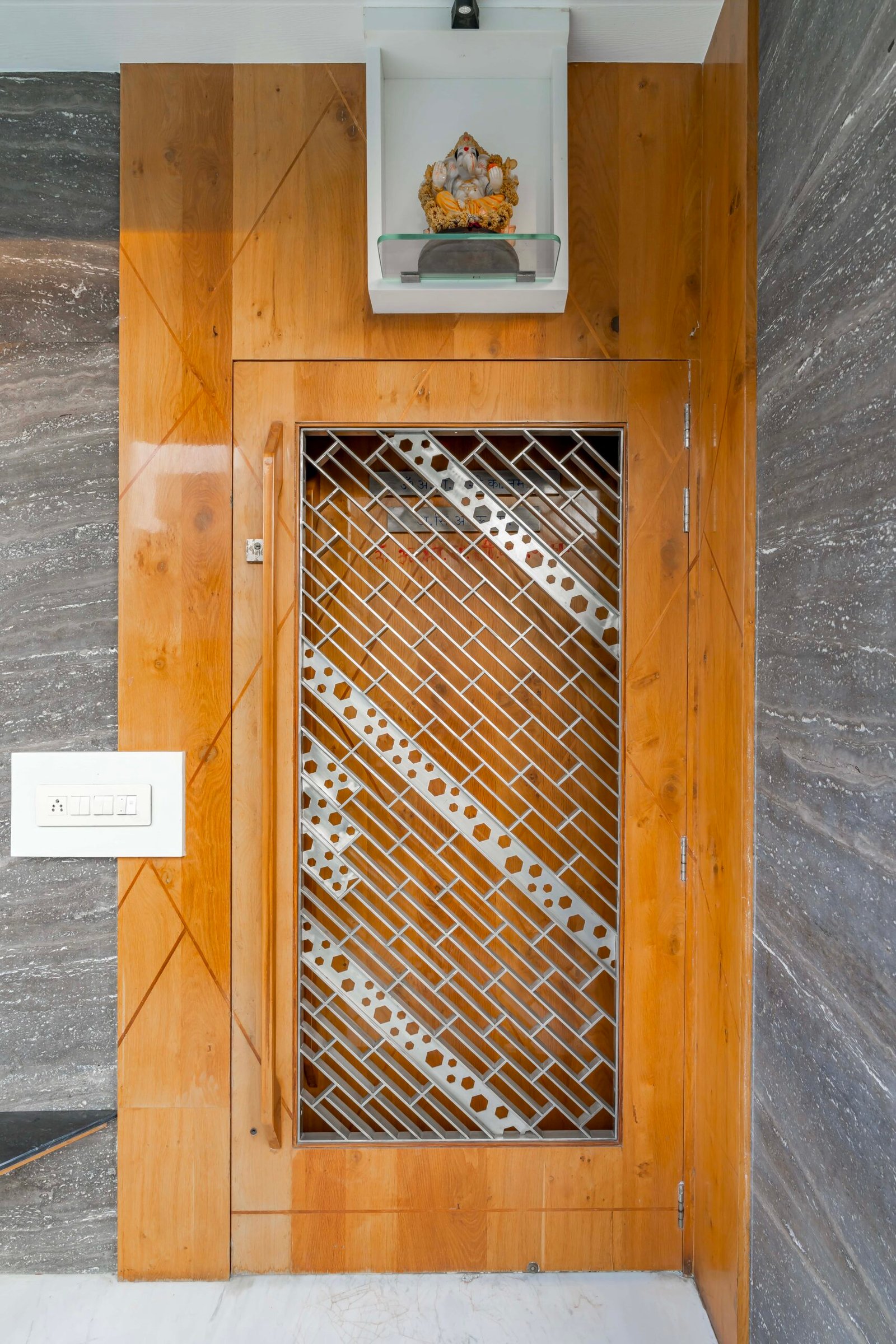 - Modern bungalow facade with exposed concrete, stone cladding, and wooden louvers in Ahmedabad - Sandstone-clad entrance with illuminated staircase and landscaped exterior - Open-plan living and dining area with geometric partition and modern chandelier - Master bedroom with blue textured wallpaper, wooden ceiling grid, and floating bedside units - Guest bedroom with geometric headboard, floating desk, and accent lighting - Polished flooring, natural wood finishes, and integrated lighting in modern residential interior