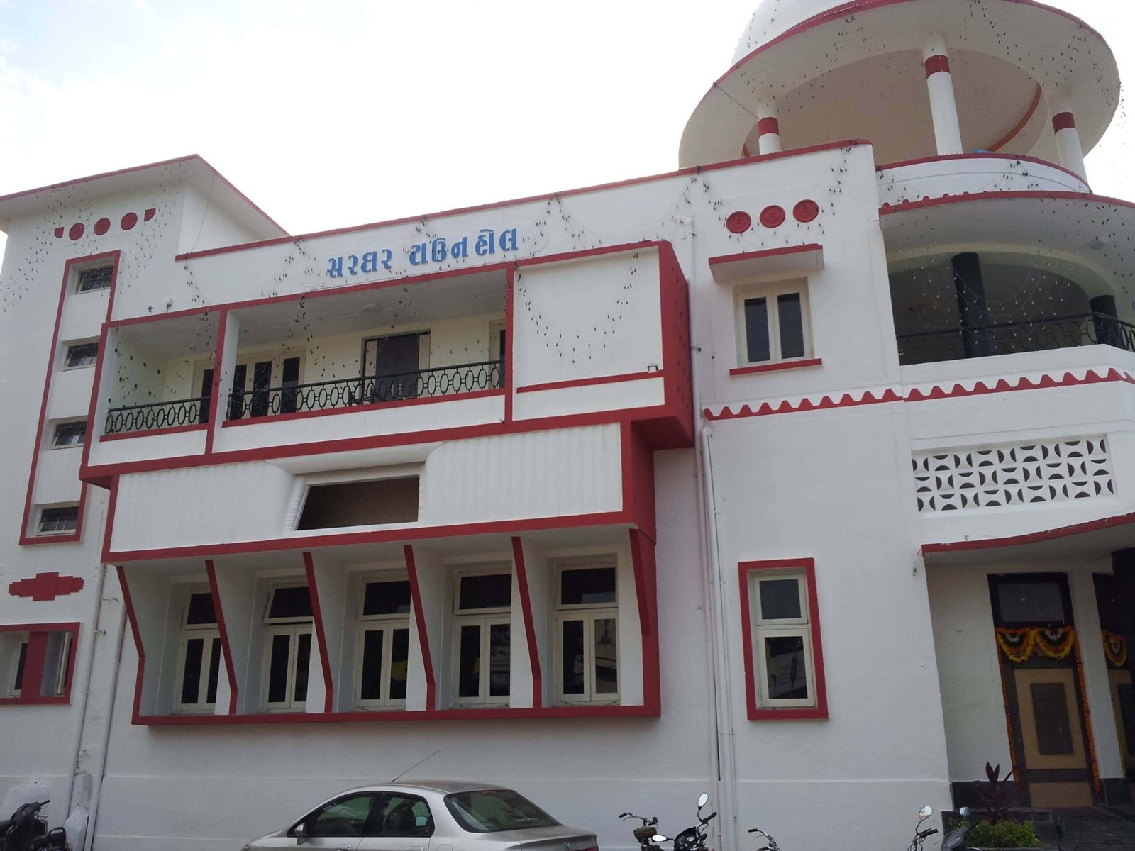 - Front elevation of the restored Sardar Townhall in Rajpipla, showcasing the heritage façade with ornate cornices and columns - Interior view of the refurbished hall with vibrant wall murals, contemporary seating, and updated lighting fixtures - Close-up of decorative plasterwork and restored wooden beams highlighting the building’s historical craftsmanship - Auditorium perspective featuring the renovated stage, modern AV equipment, and flexible seating layout - Nighttime shot of Sardar Townhall illuminated to accentuate architectural details and the entrance canopy