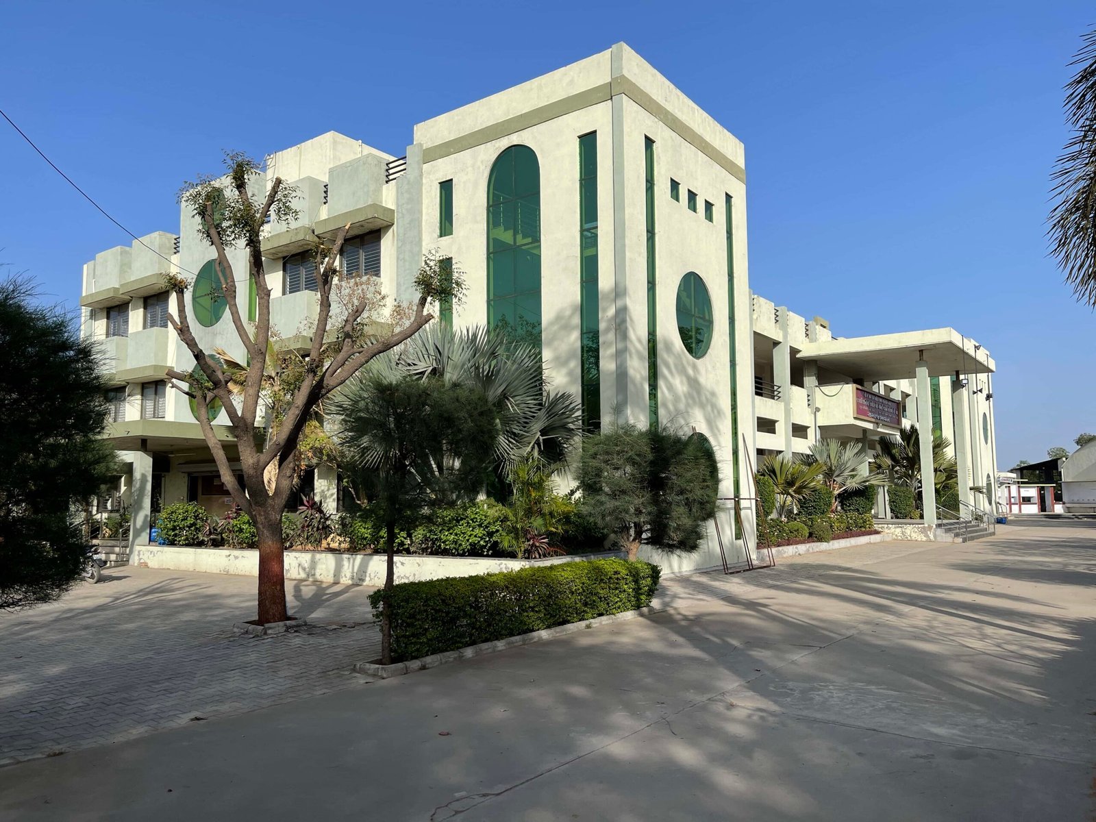 - Front elevation of the Shri 41 Gam Kadva Patidar Samaj Bhavan community building in Mansa, featuring a clean-lined modern façade with traditional Kadva Patidar motifs - Interior view of the multi-functional Community Hall showing flexible seating, natural light, and minimalist finishes - Serene Umiya Mata Temple interior with cultural carvings, prayer platform, and architectural arches - Aerial perspective of the public building’s landscaped party lawns, winding pathways, and gathering zones - Nighttime shot of the religious building illuminated to highlight the temple dome, façade details, and outdoor seating areas
