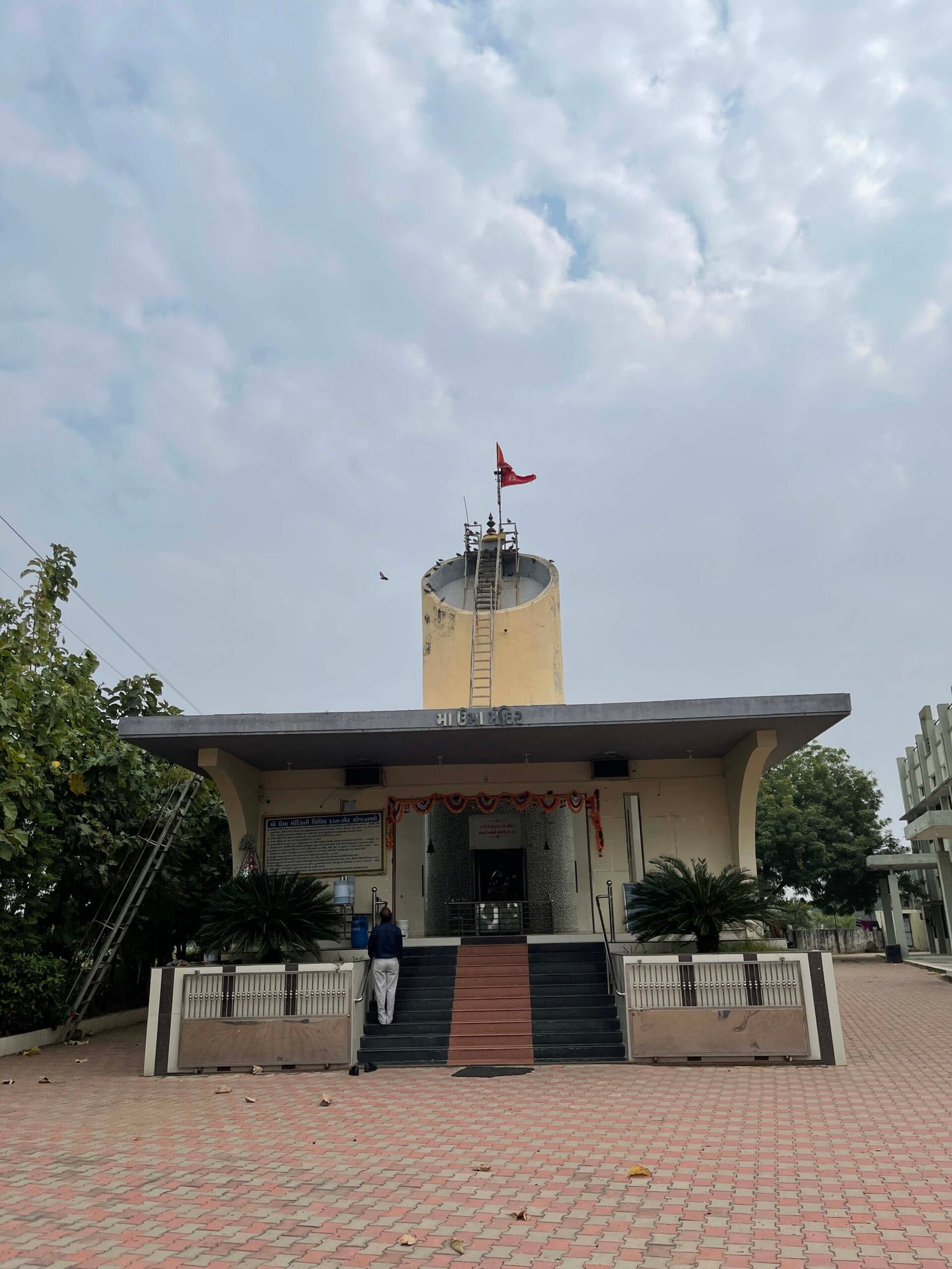 - Front elevation of the Shri 41 Gam Kadva Patidar Samaj Bhavan community building in Mansa, featuring a clean-lined modern façade with traditional Kadva Patidar motifs - Interior view of the multi-functional Community Hall showing flexible seating, natural light, and minimalist finishes - Serene Umiya Mata Temple interior with cultural carvings, prayer platform, and architectural arches - Aerial perspective of the public building’s landscaped party lawns, winding pathways, and gathering zones - Nighttime shot of the religious building illuminated to highlight the temple dome, façade details, and outdoor seating areas