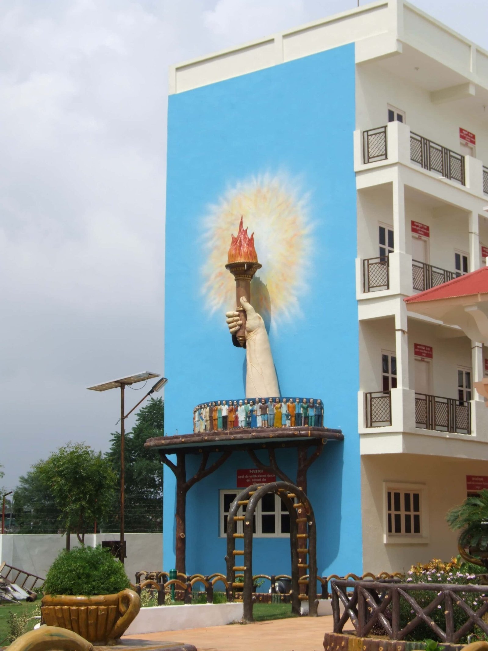 - Front view of the Gayatri Shaktipith Temple showcasing Himalayan-inspired shivalay architecture against a clear sky - Ferrocement artificial wood beams lining a landscaped pathway beside reflecting pools - Aerial perspective of the temple campus with serene gardens, pathways, and mountain-style temple roofs - Devotees walking through manicured gardens flanked by ferrocement sculptures resembling timber structures - Close-up of the shivalay temple’s ornate façade with traditional carvings and eco-centric design elements