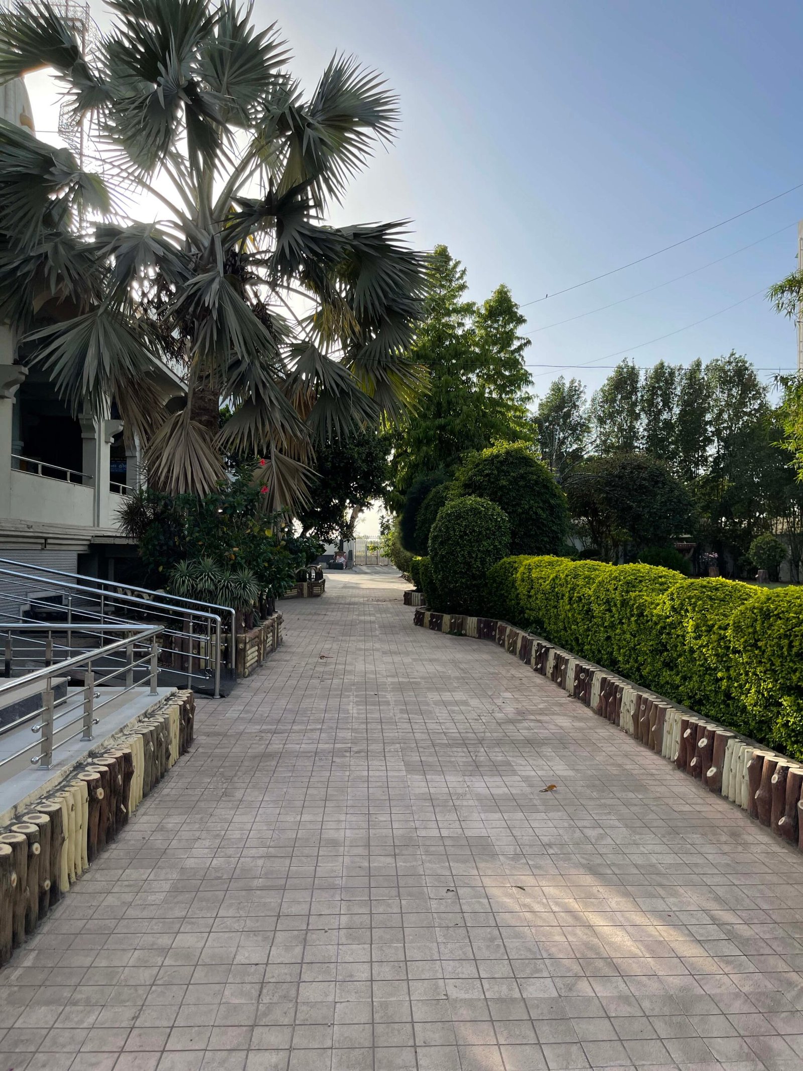 - Front view of the Gayatri Shaktipith Temple showcasing Himalayan-inspired shivalay architecture against a clear sky - Ferrocement artificial wood beams lining a landscaped pathway beside reflecting pools - Aerial perspective of the temple campus with serene gardens, pathways, and mountain-style temple roofs - Devotees walking through manicured gardens flanked by ferrocement sculptures resembling timber structures - Close-up of the shivalay temple’s ornate façade with traditional carvings and eco-centric design elements