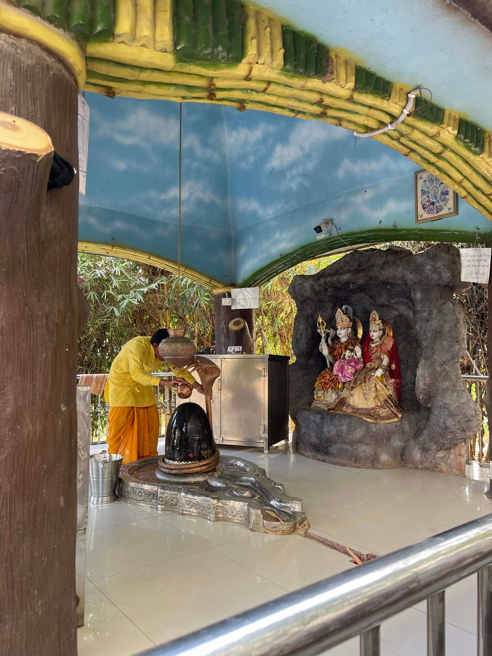 - Front view of the Gayatri Shaktipith Temple showcasing Himalayan-inspired shivalay architecture against a clear sky - Ferrocement artificial wood beams lining a landscaped pathway beside reflecting pools - Aerial perspective of the temple campus with serene gardens, pathways, and mountain-style temple roofs - Devotees walking through manicured gardens flanked by ferrocement sculptures resembling timber structures - Close-up of the shivalay temple’s ornate façade with traditional carvings and eco-centric design elements