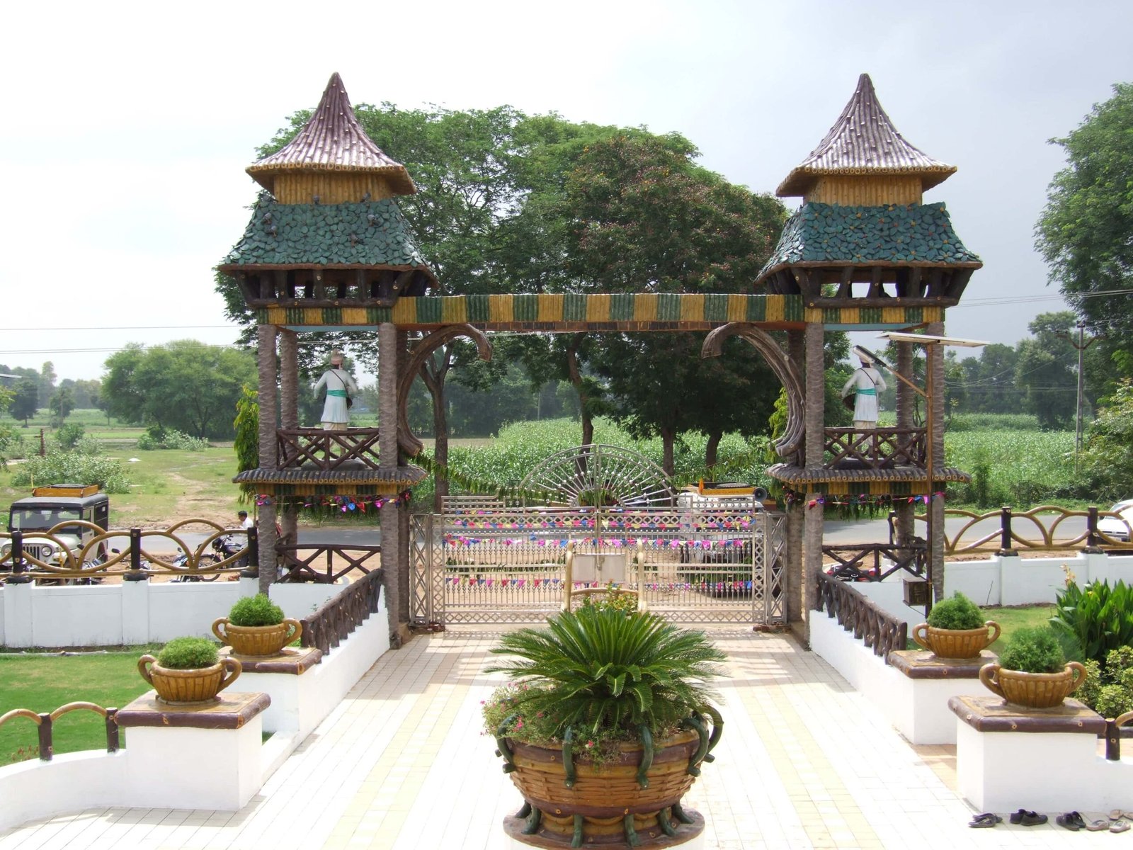 - Front view of the Gayatri Shaktipith Temple showcasing Himalayan-inspired shivalay architecture against a clear sky - Ferrocement artificial wood beams lining a landscaped pathway beside reflecting pools - Aerial perspective of the temple campus with serene gardens, pathways, and mountain-style temple roofs - Devotees walking through manicured gardens flanked by ferrocement sculptures resembling timber structures - Close-up of the shivalay temple’s ornate façade with traditional carvings and eco-centric design elements