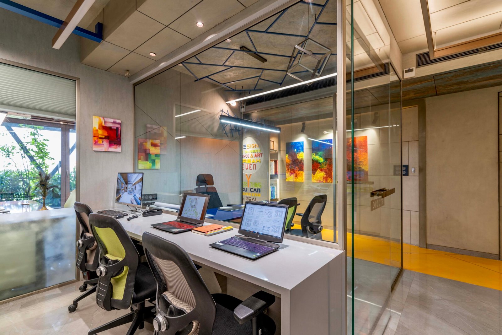 -Exterior shot of Vastu Nirman Architects’ Office in Ahmedabad featuring a minimalist façade, green planter boxes, and entrance signage -Reception area with vibrant accent wall, sleek minimalist desk, and eco-friendly décor elements -Open-plan collaborative workspace showing adjustable desks, colorful partitions, and abundant natural light -Living wall installation and indoor plant clusters creating a green oasis within the office interior -Flexible brainstorming zone with modular seating, writable wall panels, and sustainable lighting fixtures