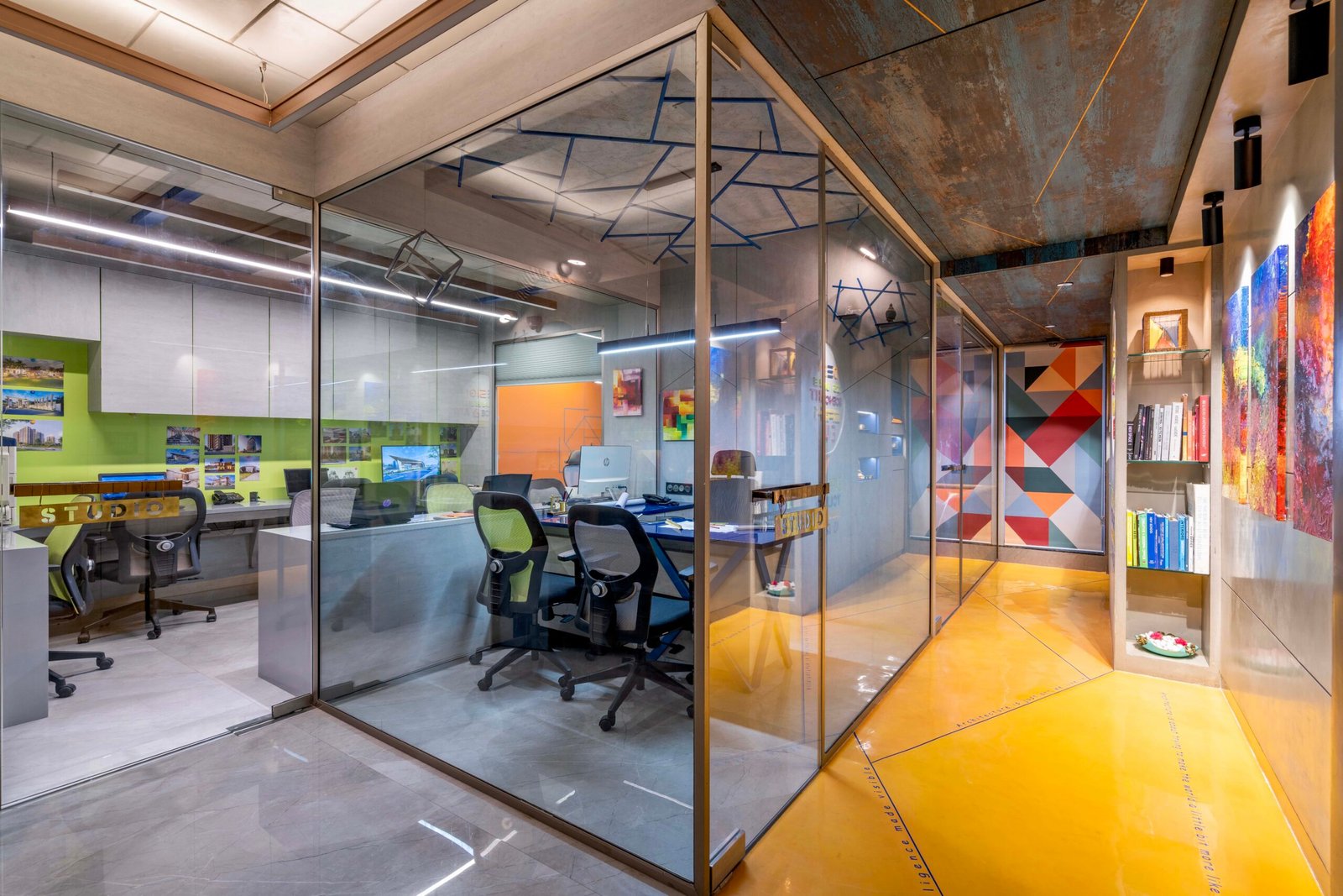 -Exterior shot of Vastu Nirman Architects’ Office in Ahmedabad featuring a minimalist façade, green planter boxes, and entrance signage -Reception area with vibrant accent wall, sleek minimalist desk, and eco-friendly décor elements -Open-plan collaborative workspace showing adjustable desks, colorful partitions, and abundant natural light -Living wall installation and indoor plant clusters creating a green oasis within the office interior -Flexible brainstorming zone with modular seating, writable wall panels, and sustainable lighting fixtures