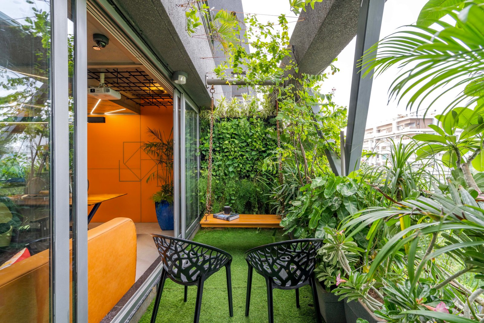 -Exterior shot of Vastu Nirman Architects’ Office in Ahmedabad featuring a minimalist façade, green planter boxes, and entrance signage -Reception area with vibrant accent wall, sleek minimalist desk, and eco-friendly décor elements -Open-plan collaborative workspace showing adjustable desks, colorful partitions, and abundant natural light -Living wall installation and indoor plant clusters creating a green oasis within the office interior -Flexible brainstorming zone with modular seating, writable wall panels, and sustainable lighting fixtures