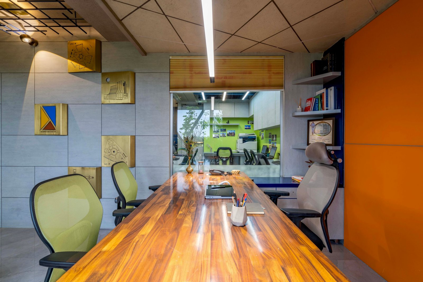 -Exterior shot of Vastu Nirman Architects’ Office in Ahmedabad featuring a minimalist façade, green planter boxes, and entrance signage -Reception area with vibrant accent wall, sleek minimalist desk, and eco-friendly décor elements -Open-plan collaborative workspace showing adjustable desks, colorful partitions, and abundant natural light -Living wall installation and indoor plant clusters creating a green oasis within the office interior -Flexible brainstorming zone with modular seating, writable wall panels, and sustainable lighting fixtures